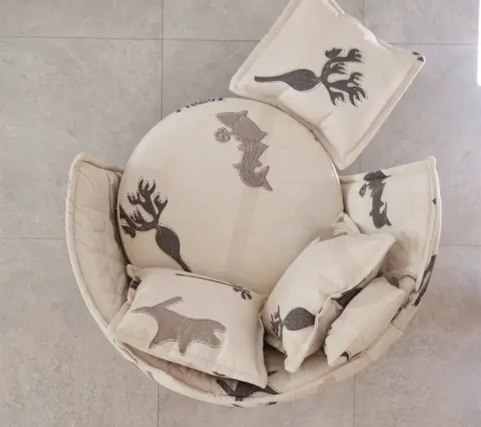 Vista superior de sillón y puff tapizado en tela Quetzal, un tejido claro con motivos decorativos en tonos grises, acompañada de varios cojines a juego.
