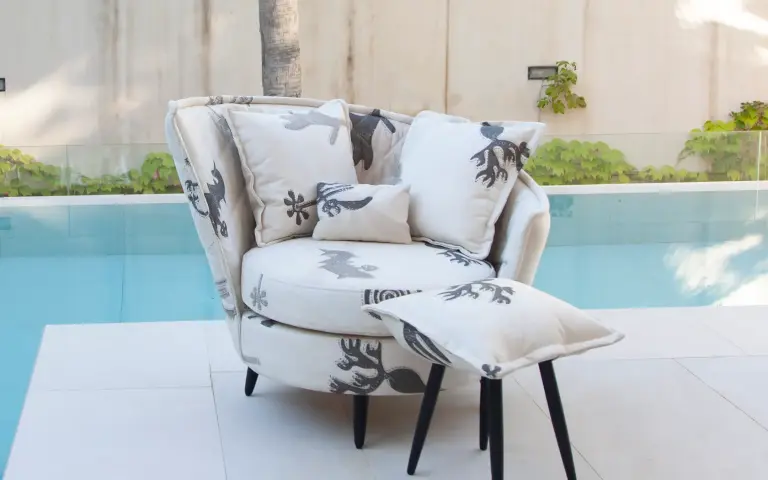 Sillón tapizado en tela Quetzal, un tejido claro con motivos decorativos en tonos grises, acompañado de cojines a juego junto a una piscina exterior.