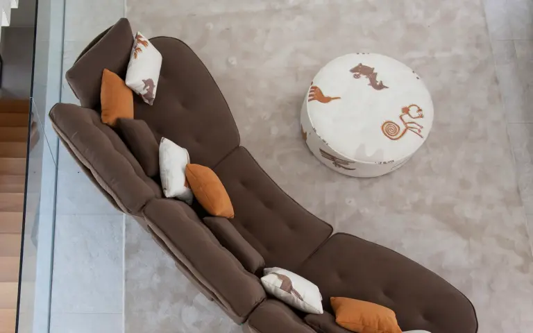 Vista superior de sofá modular marrón combinado con puff tapizado en tela Quetzal, un tejido claro con motivos decorativos en tonos tierra, en un salón contemporáneo.