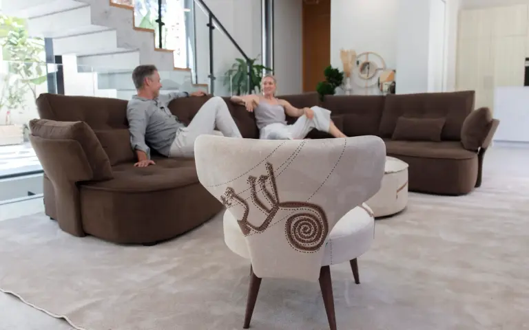 Silla tapizada en tela Quetzal, un tejido claro con motivos decorativos en tonos tierra, combinada con un sofá modular marrón en un salón moderno y luminoso.
