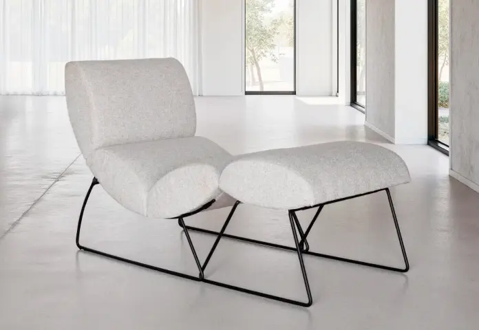 Sillón Neox de Fama Sofás con diseño chaise, respaldo envolvente y base metálica, en tejido color crudo.